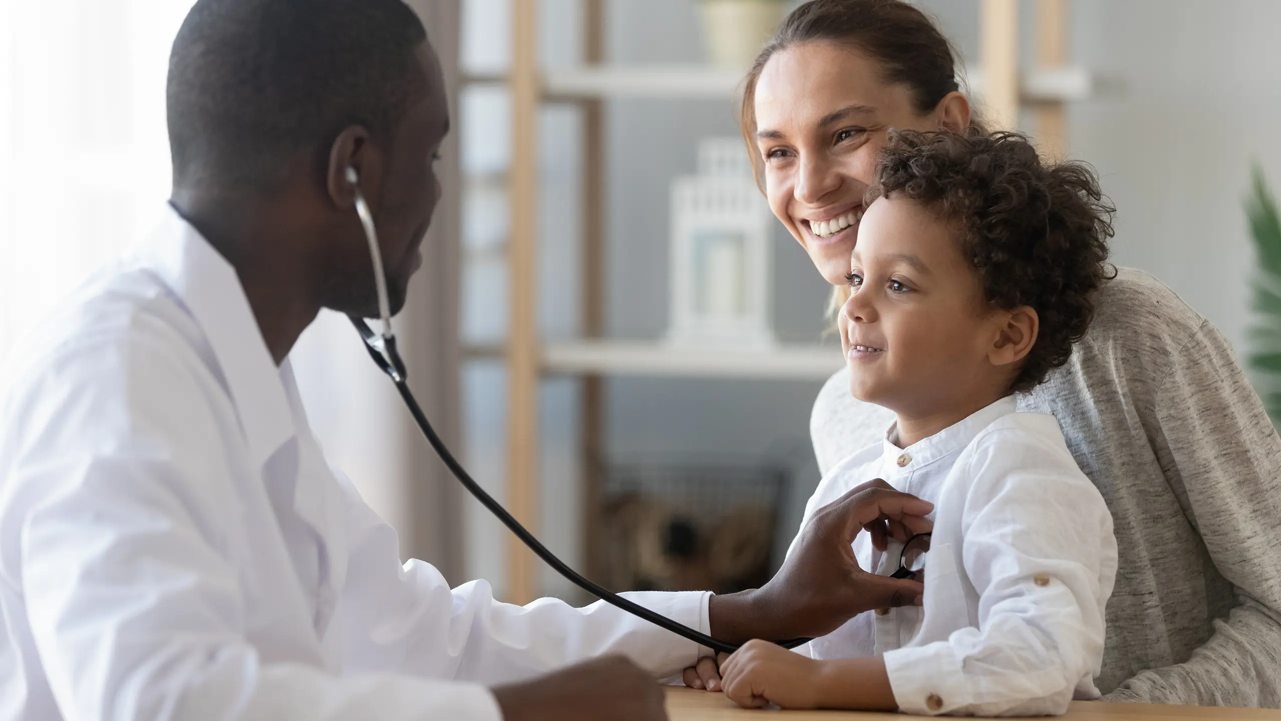 African American doctor with a stethoscope examining a smiling child and mother