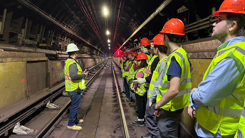 Students wearing yellow reflective vests and orange hardhats participating with Bloustein Enthusiasts and Advocates for Transportation (BEAT) took part in an exclusive after-hours PATH (Port Authority Trans-Hudson) tour.